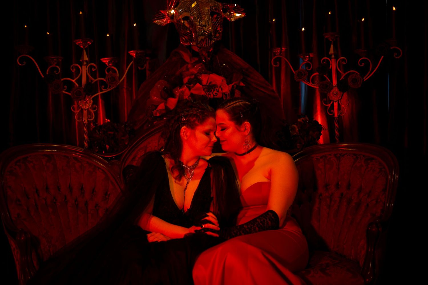 A lesbian couple snuggle together on a velvet couch on their wedding day.