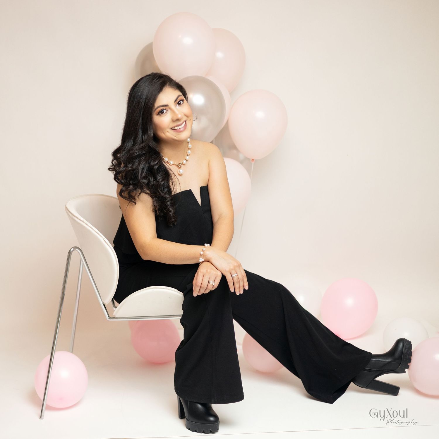 Woman in black dress poses elegantly with pink balloons against white backdrop in boudoir photoshoot series.