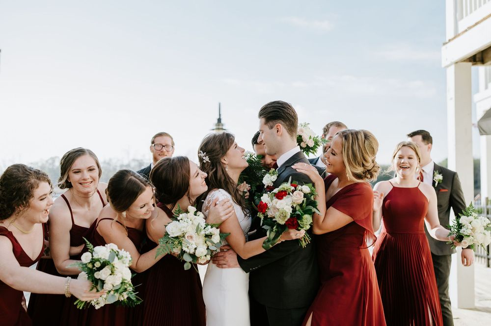 Wedding party wearing black and burgundy attire share joyful moments together in a candid group photo.