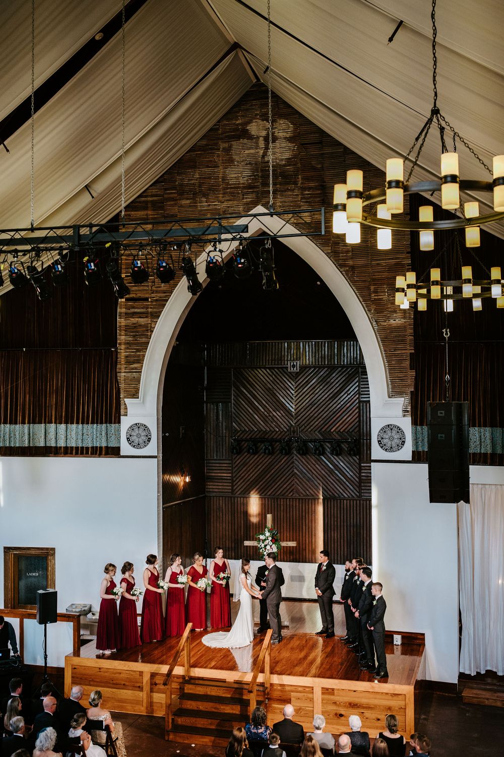 A wedding ceremony setup in a rustic venue with wooden benches and hanging pendant lights creating an intimate atmosphere.