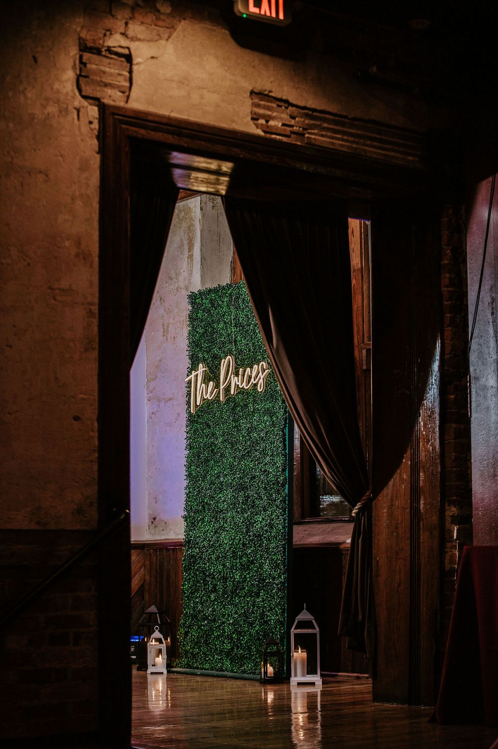 A dimly lit venue space features a green hedge wall backdrop with glowing lanterns and an illuminated sign.
