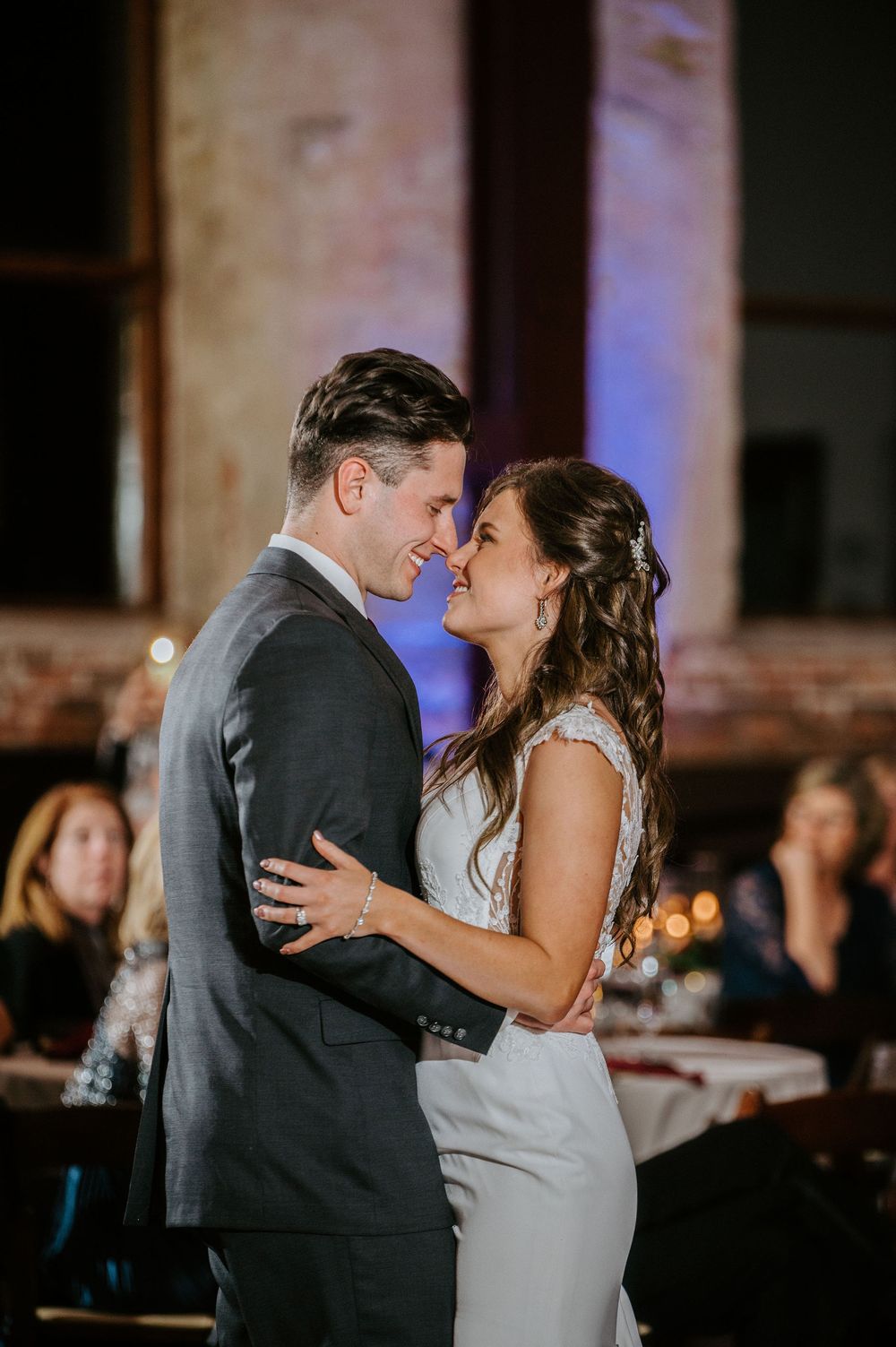 A couple shares a romantic first dance together at their wedding reception in a dimly lit venue with blue lighting.