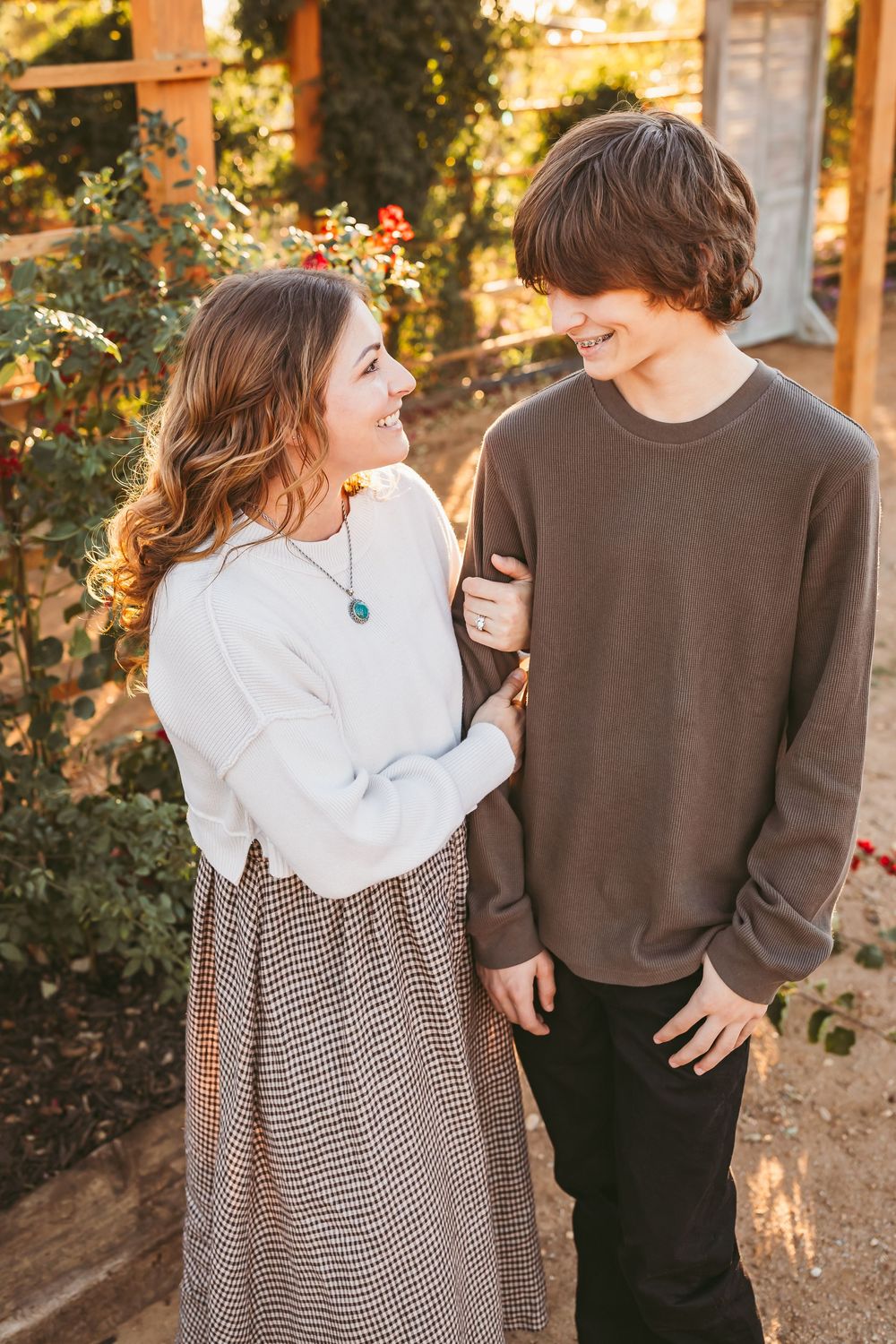A couple in casual sweaters walking together in a garden during golden hour sunset.