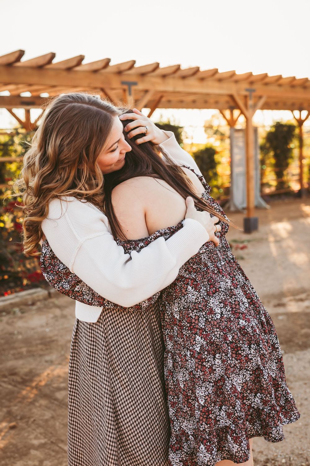 Two people in coordinating outfits embrace during a golden sunset photoshoot under a wooden pergola.