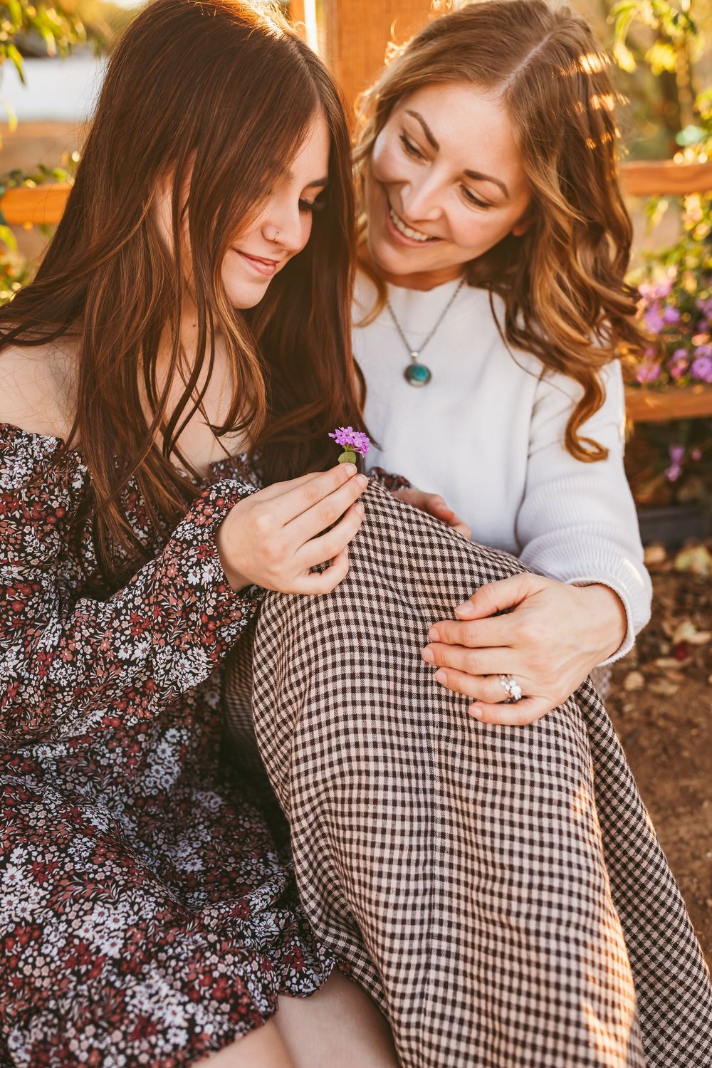 A daughter and her mom share a cuddle moment in floral and gingham prints against a warm sunset backdrop at a ranch in Cherry Valley.