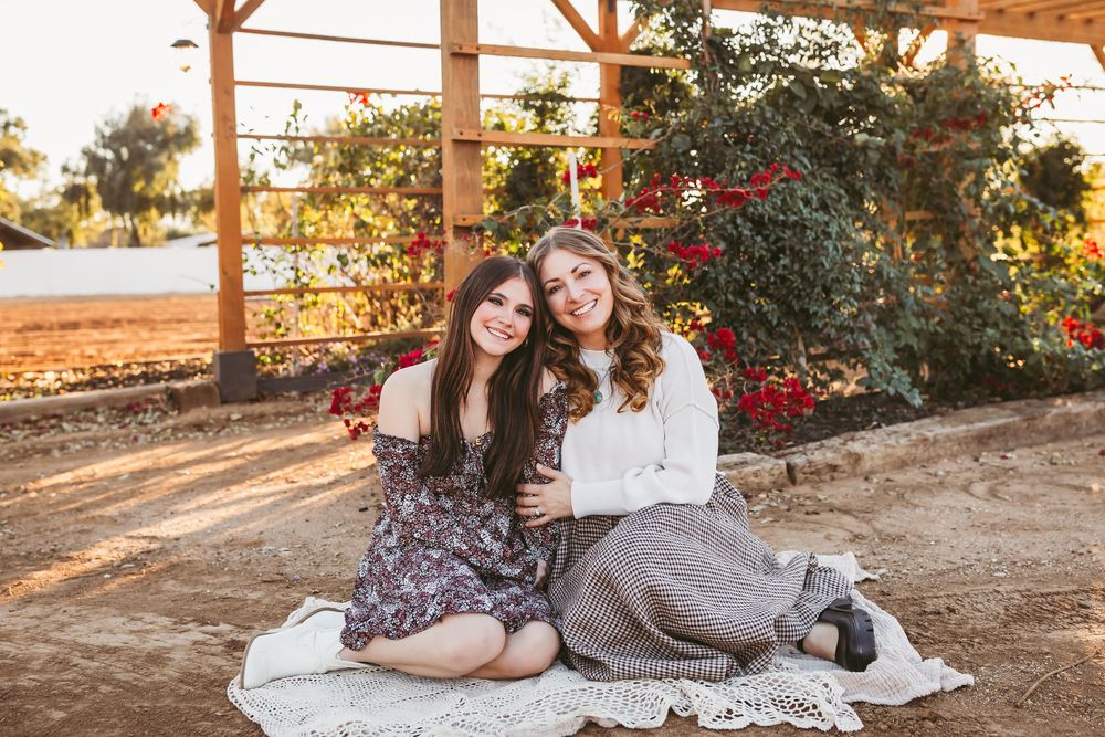A couple sits together on a white blanket in a rustic outdoor setting during golden hour.