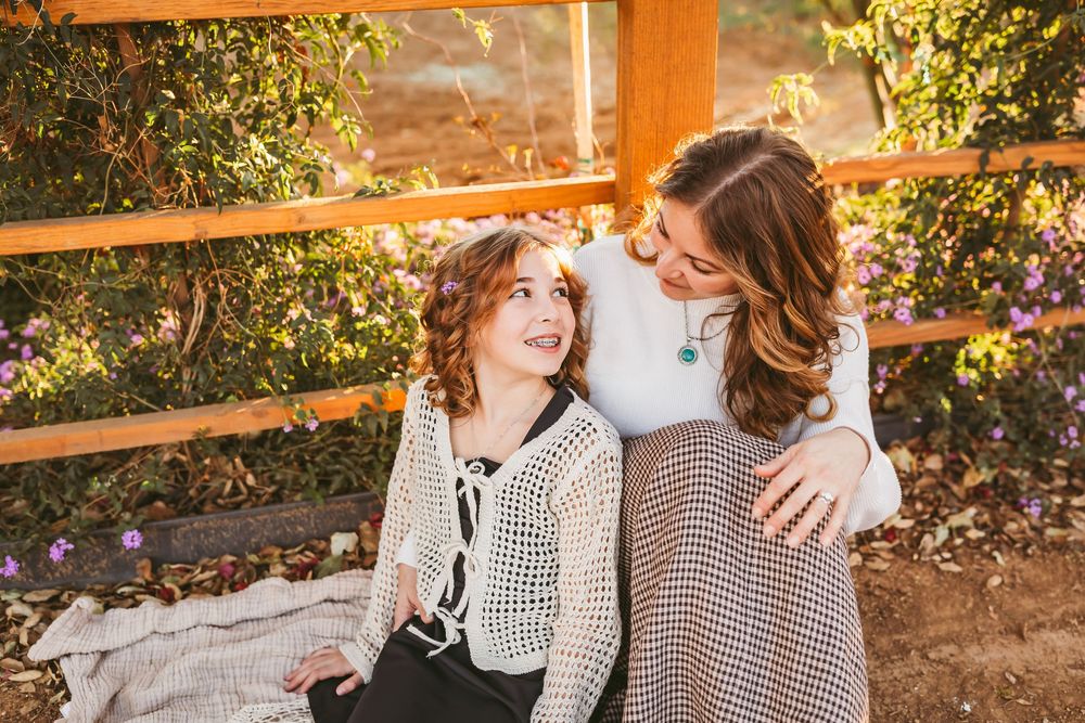A couple in matching gingham shirts laughs together during a golden hour photo session in a garden setting.