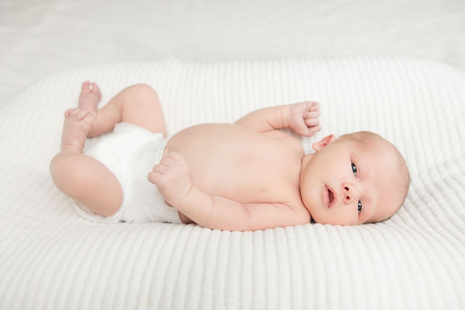 A newborn baby lying on white bedding in four different poses showing peaceful sleeping and alert moments.