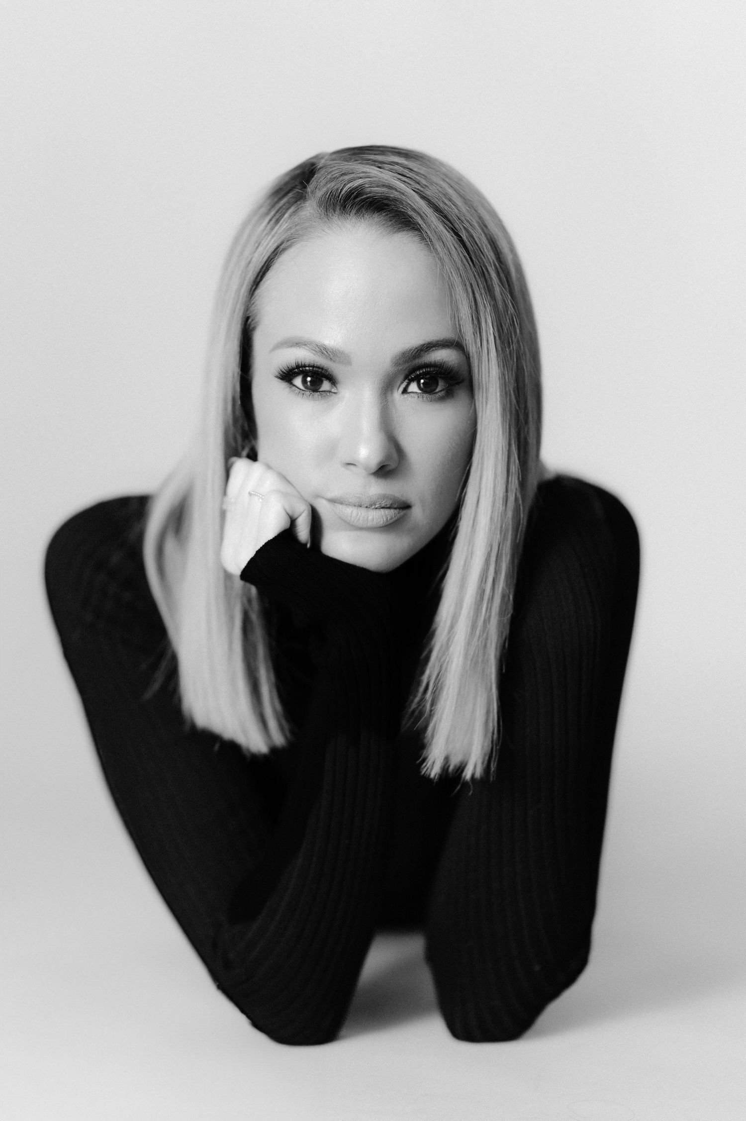 Professional headshot of a blonde woman in black turtleneck against white background.