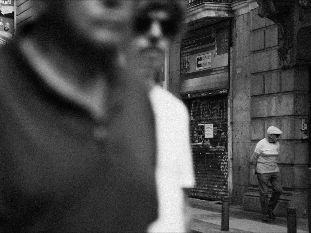 A black and white photograph showing a blurry, out-of-focus urban street scene with buildings in the background.