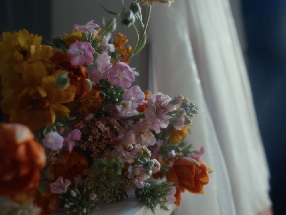 A vibrant floral arrangement with orange, pink and purple blooms sits elegantly against a white curtained backdrop.