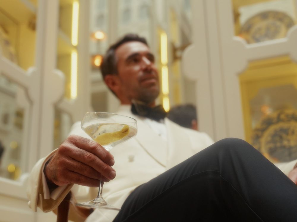 A person holds a glass of wine in an elegant restaurant setting with ornate decor and golden lighting.