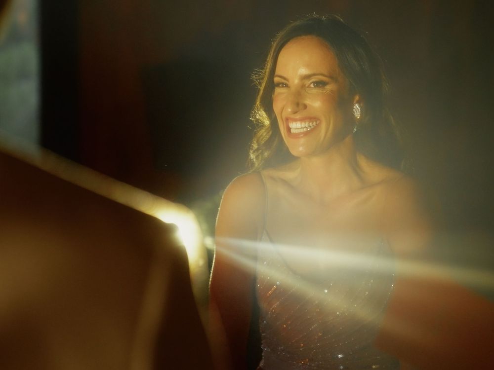 A person in a red dress smiles warmly while bathed in soft golden lighting with lens flare effects.