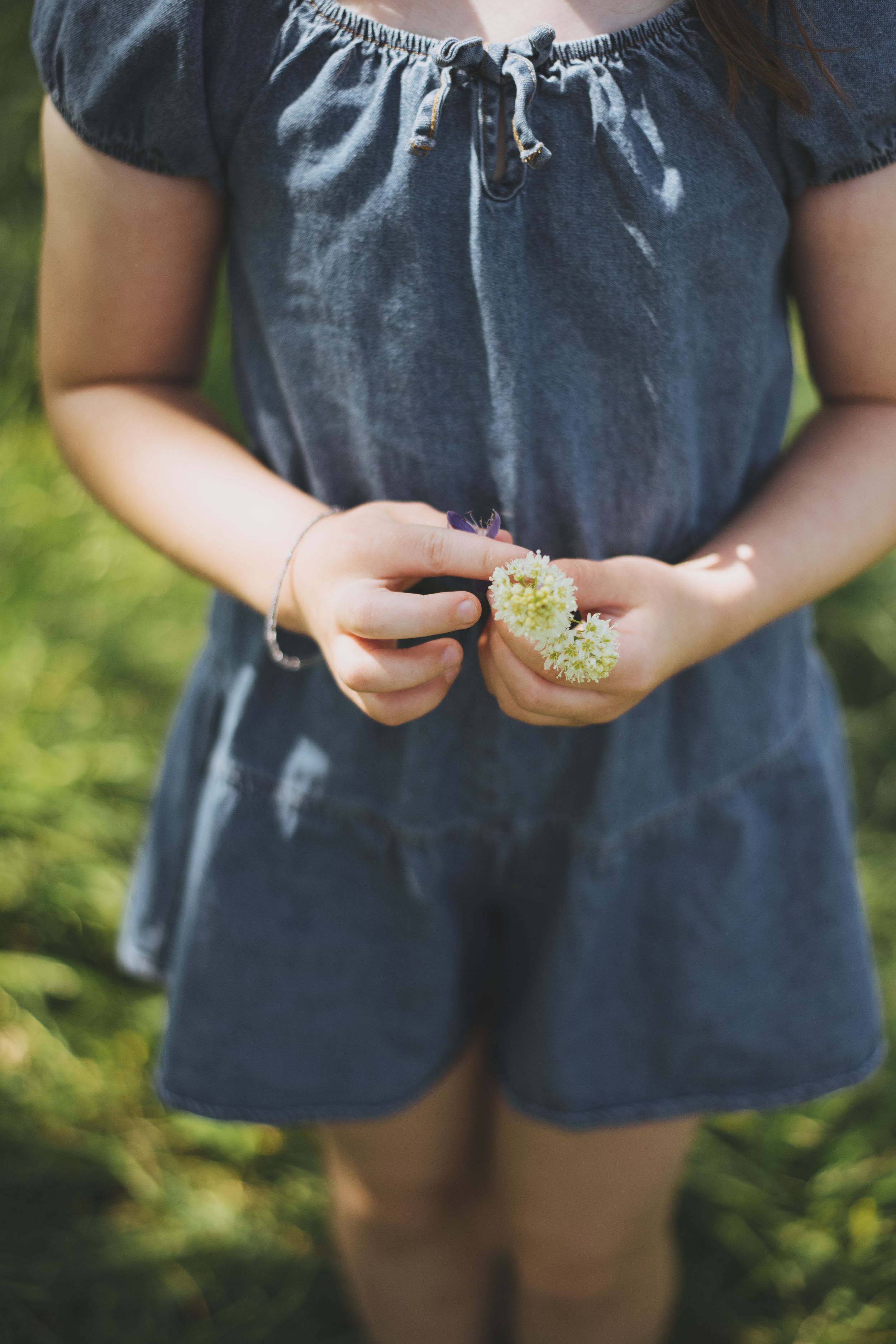 Close-up view of hands holding small white flowers against a dark blue romper background outdoors.
