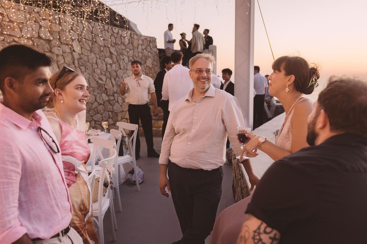Santorini Destination wedding guests dance and socialise at an outdoor reception during sunset with stone walls at El Viento.