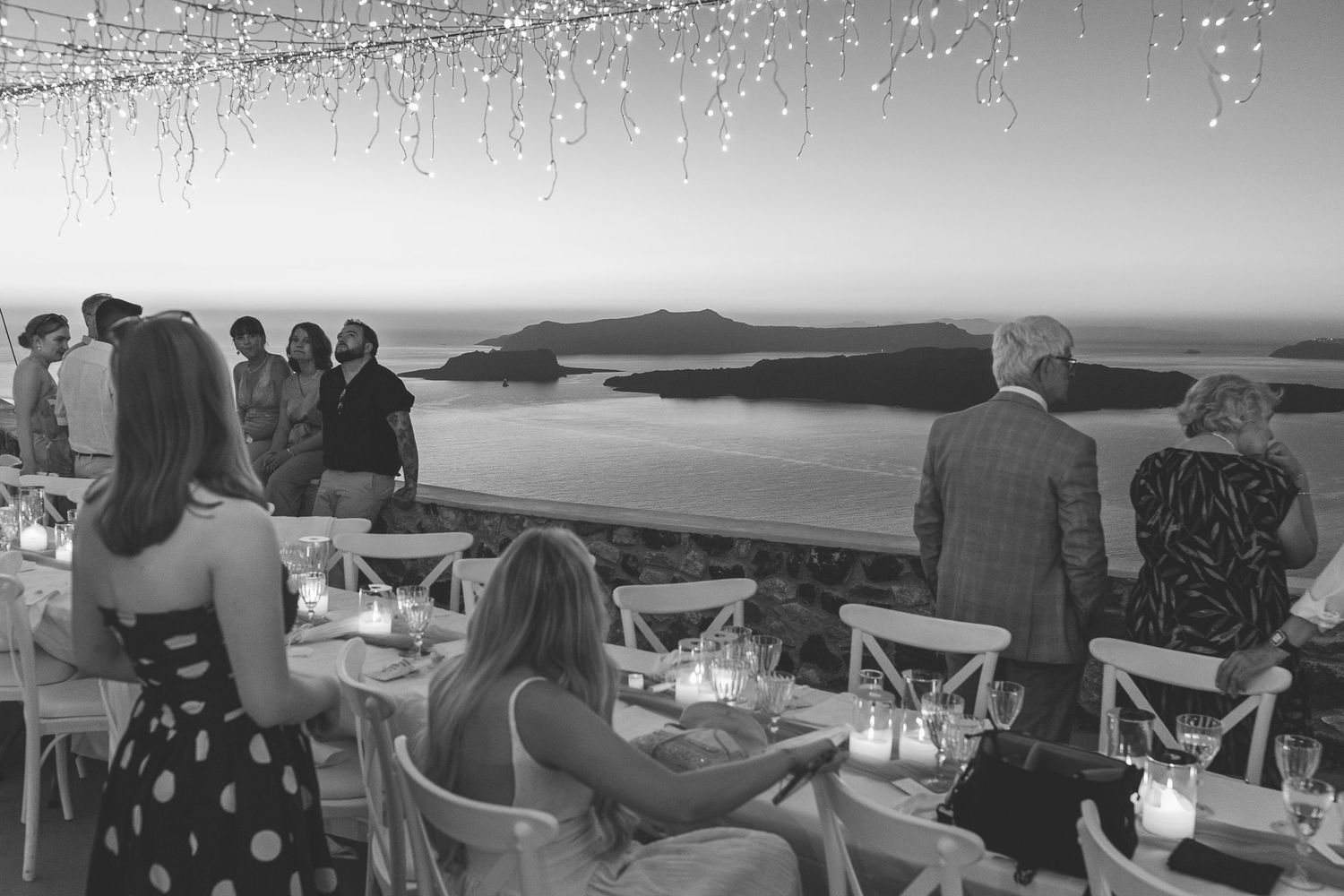 Destination wedding guests around a long table with scenic Santorini views at sunset.