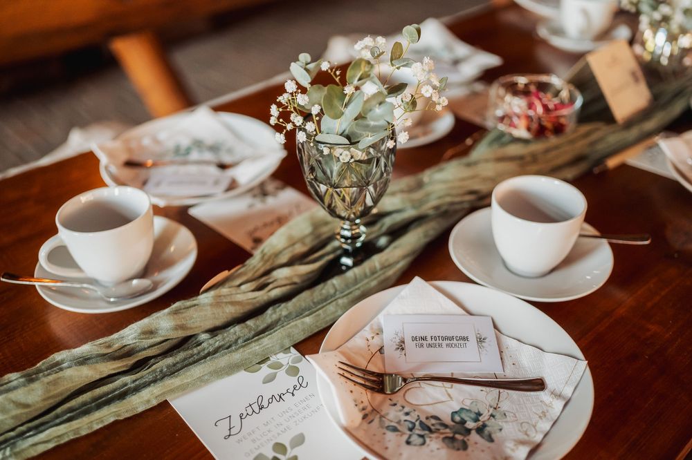 Elegant table settings with white teacups and floral centerpieces at a rustic wedding reception.