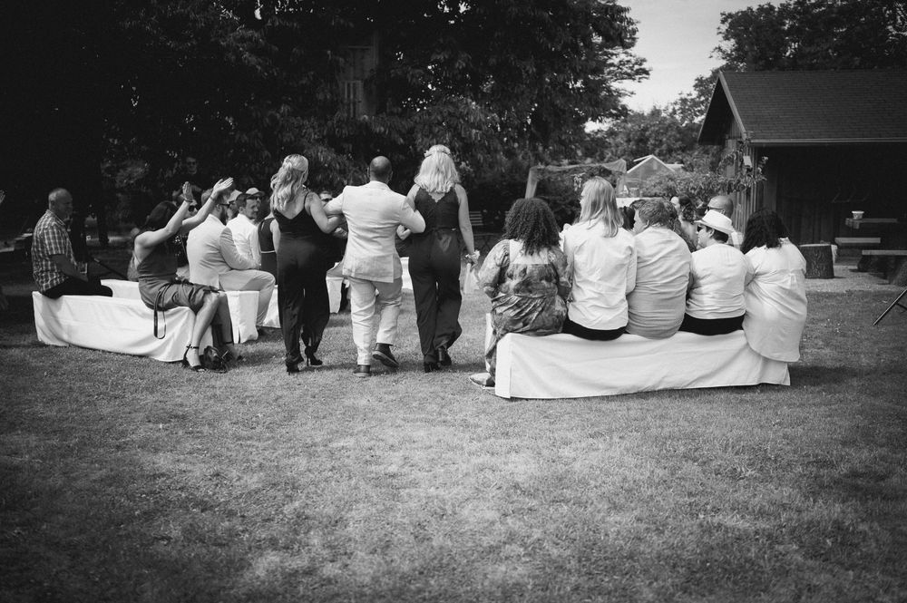 Wedding party sits together on grass in casual outdoor setting during summer celebration.