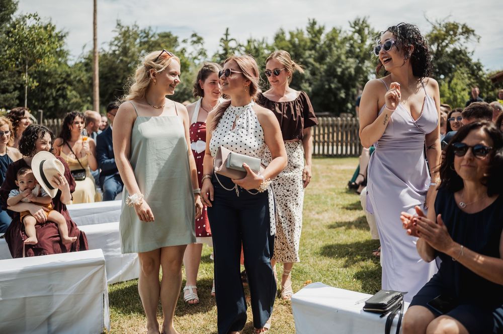A group of guests enjoying a sunny outdoor celebration on a grassy lawn with white seating.