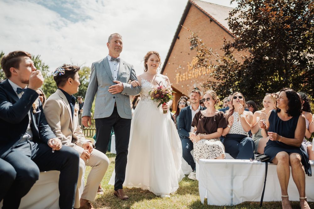 Wedding party and guests mingling outdoors on a grassy area during a summer celebration.