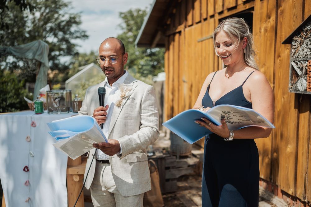 A couple stands at a podium during an outdoor ceremony in front of a rustic wooden barn.