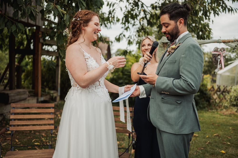 Bride and groom share a tender moment during their wedding ceremony under trees in natural light.