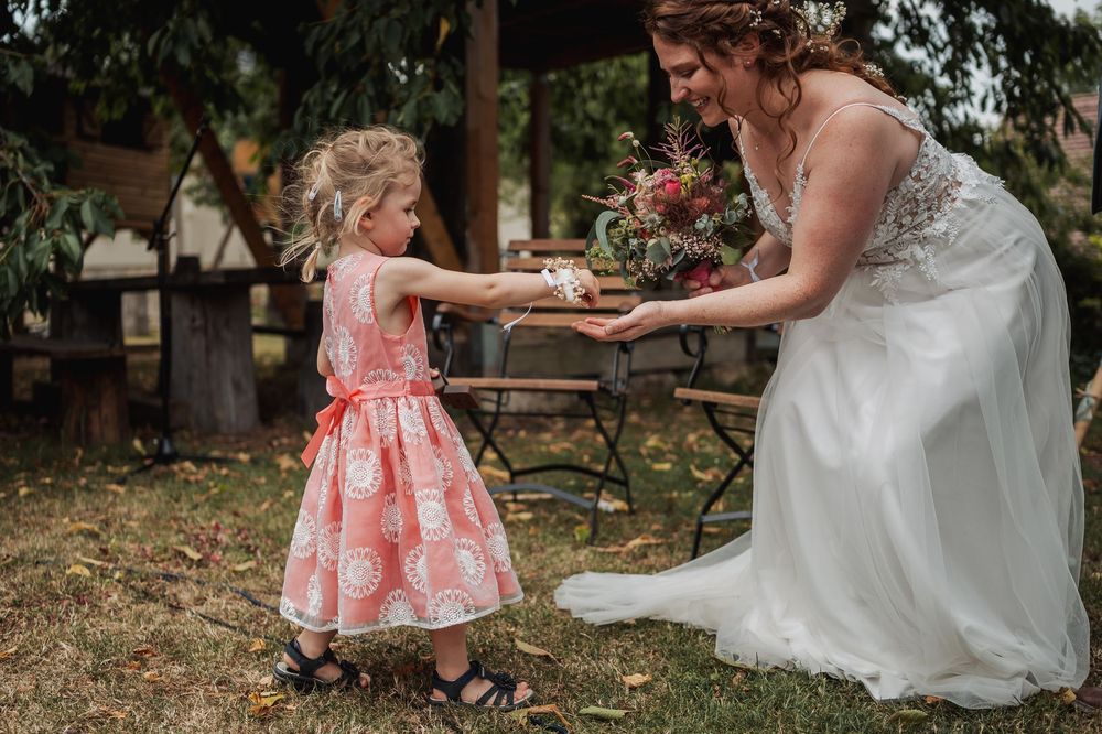 A young attendee in a coral dress twirls with a bride in a white gown during an outdoor celebration.
