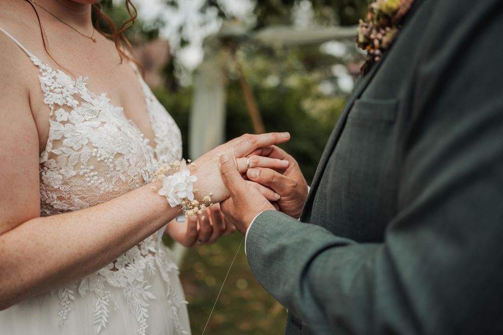 Close-up of hands holding during outdoor wedding ceremony with lace dress detail visible.
