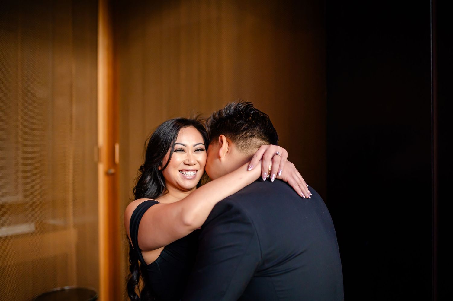 A couple shares an intimate moment during their engagement photo session in a warmly lit indoor setting.