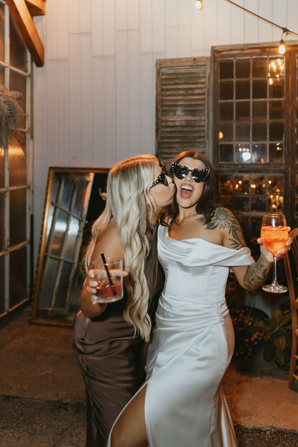 Wedding guests enjoying cocktails and dancing at an evening reception with rustic wooden decor and warm lighting.