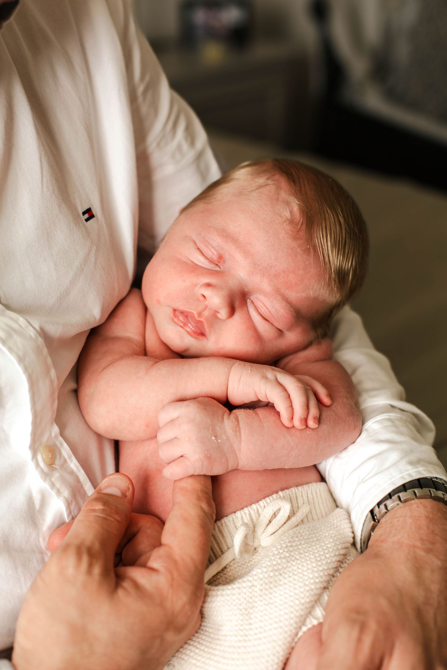 A newborn baby sleeps peacefully on soft white blankets in a series of connected photographs.