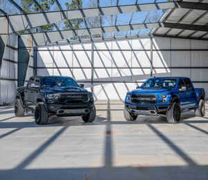 Blue Ford Raptor and Dodge Ram TRX in a parking structure with sunlight casting shadows through the roof in Charleston, SC.