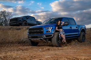 Blue Ford Raptor and black Dodge Ram TRX pickup truck parked on dirt terrain at sunset with dramatic cloudy sky in Charleston, SC .