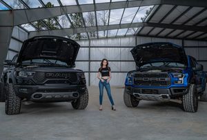 Model posing for a portrait session between a Ford Raptor and Dodge Ram TRX inside a large metal garage in Charleston, SC.