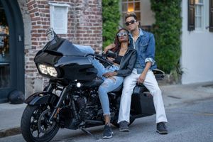 A model couple poses next to a custom black Harley Davidson Road Glide on a cobblestone street in Charleston, SC.