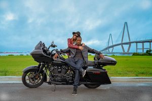 A couple posing with a Harley Davidson Road Glide motorcycle parked across from the Ravenal Bridge in Charleston, SC.