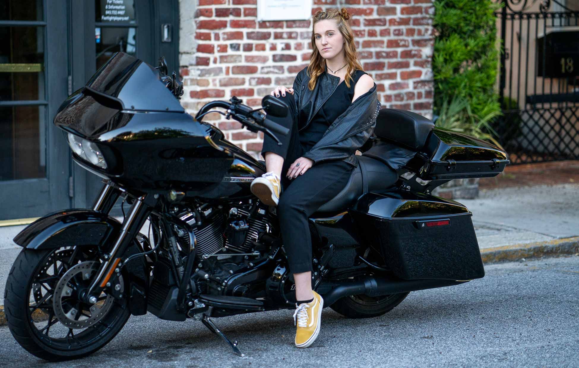 A row sleek black Harley Davidson Roadglide motorcycle parked along a brick wall with model posing in all black in Charleston, SC