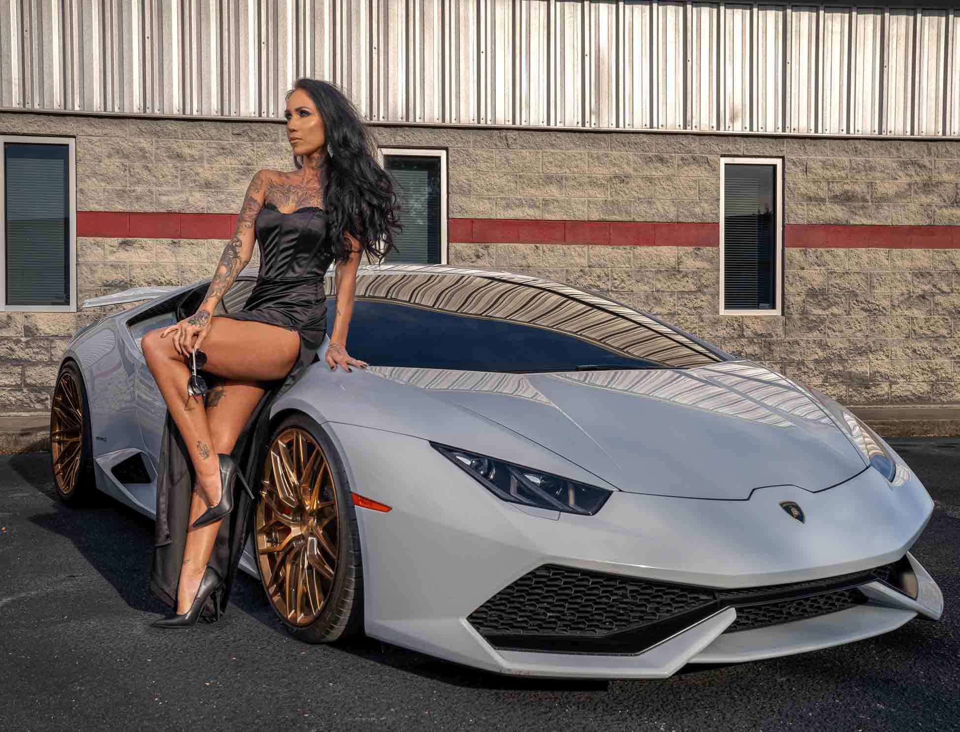 White Lamborghini Huracan with bronze wheels parked in front of industrial building with model in black dress posing in Columbia, SC.