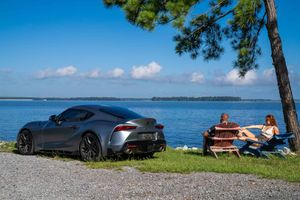 A couple posing with their Toyota Supra at scenic waterfront in Monks Corner, SC with trees and blue sky in the background.