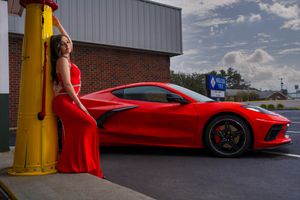 A bright red Corvette C8 sports car is displayed a vintage gas station with model posing in red dress at sunset in Charleston, SC