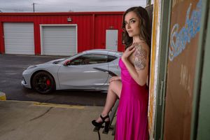 Model posing for portrait in bright pink dress with a Corvette C8 in the background. Located in Charleston, SC industrial area