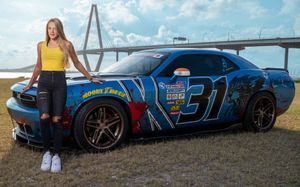 A model poses with a blue Dodge Challenger parked in front of the Ravenal Bridge against a blue sky background in Charleston, SC.