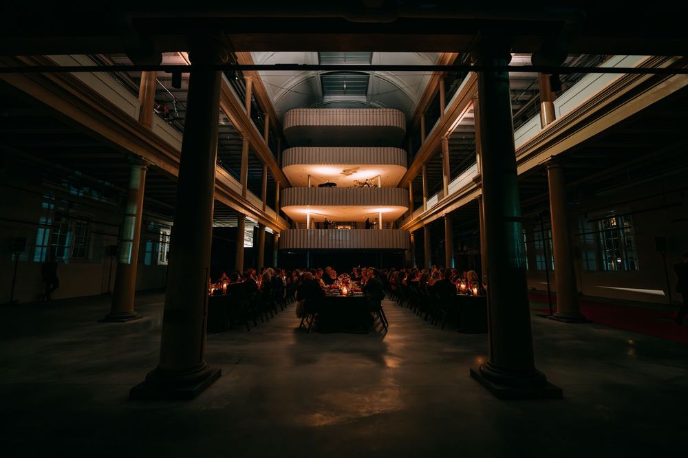 Dark and moody industrial warehouse interior with dramatic lighting and architectural columns creates atmospheric ambiance.