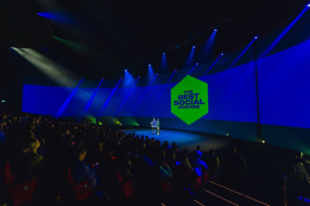 Colorful concert stage lighting with blue and green beams illuminating a dark venue during a performance.