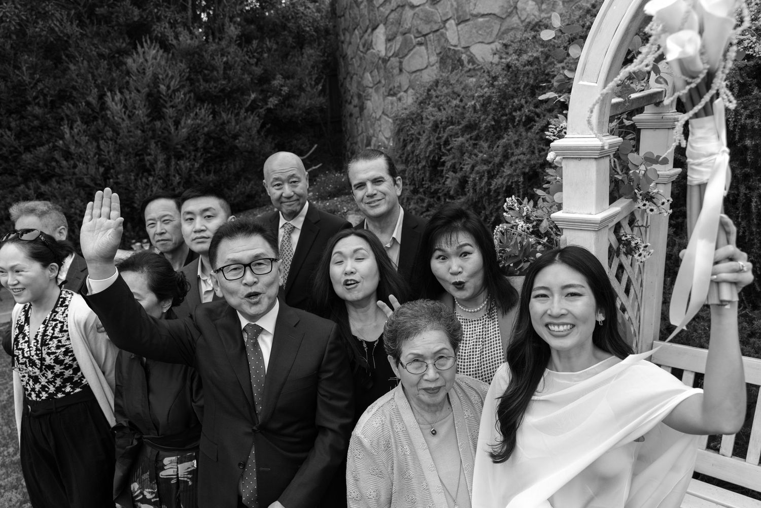 A group of wedding guests gather outdoors for formal photos during a celebration.