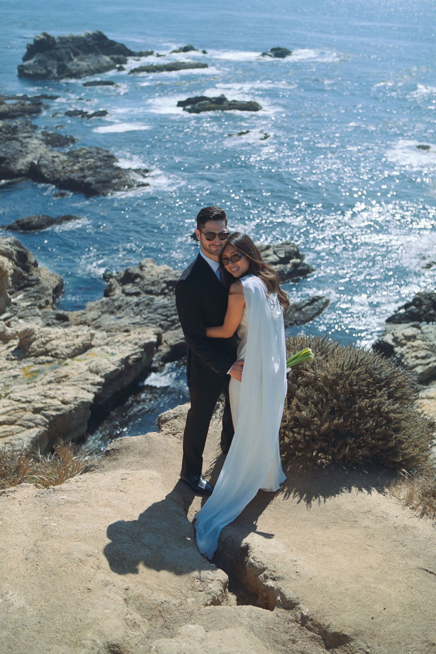 Scenic coastal cliffside overlooking blue ocean waters with rocky outcrops and sparkling sunlight.