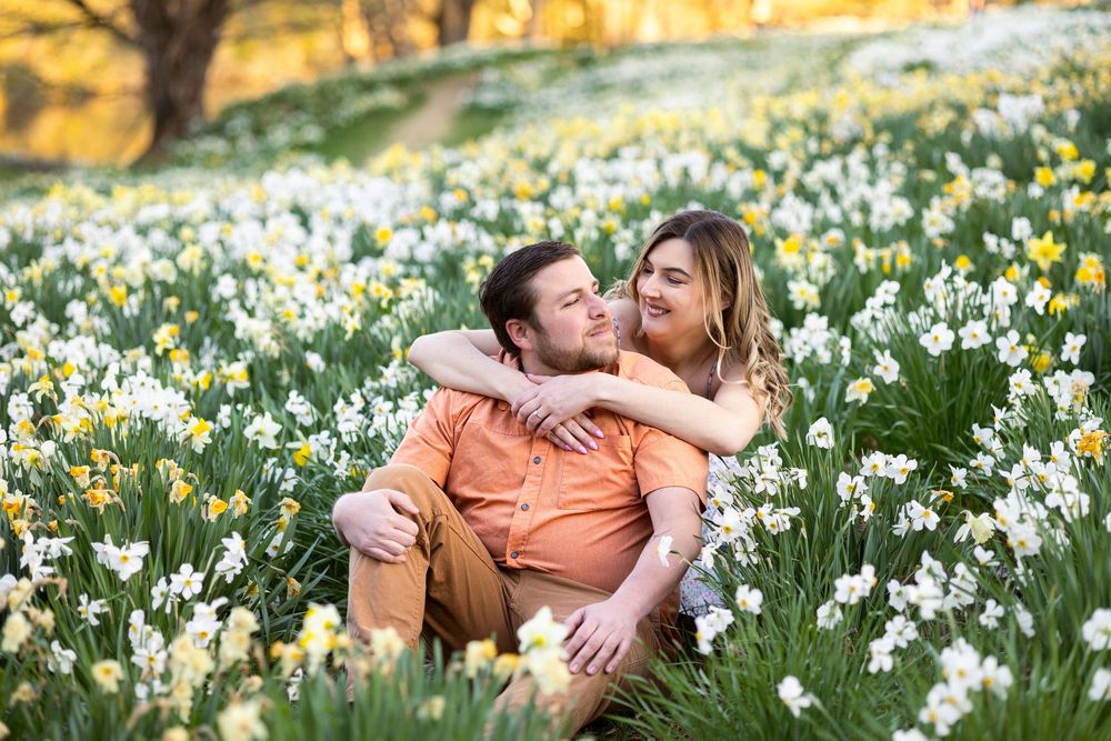 A couple embraces in a spring meadow filled with blooming white daffodils at sunset.