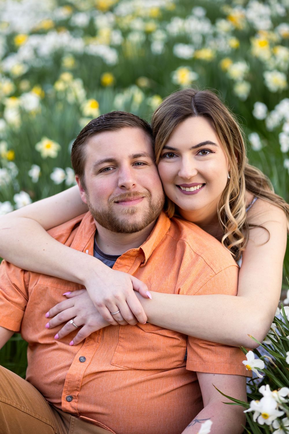 A couple embraces in a field of blooming daisies on a sunny spring day.