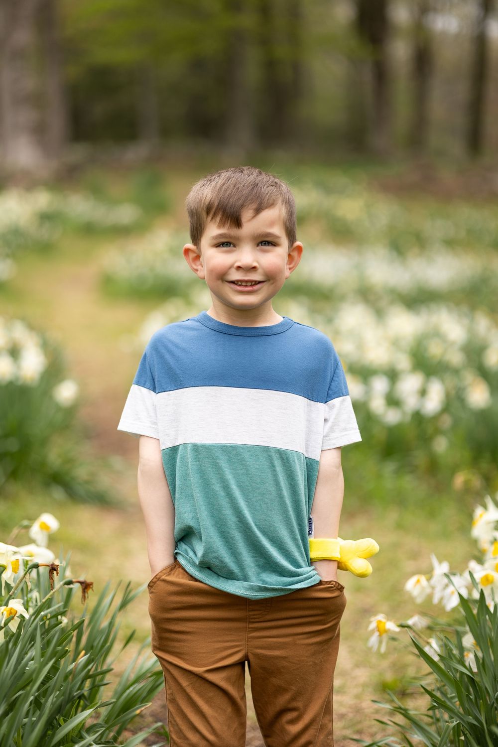 A young child poses cheerfully among spring daffodils in casual attire.