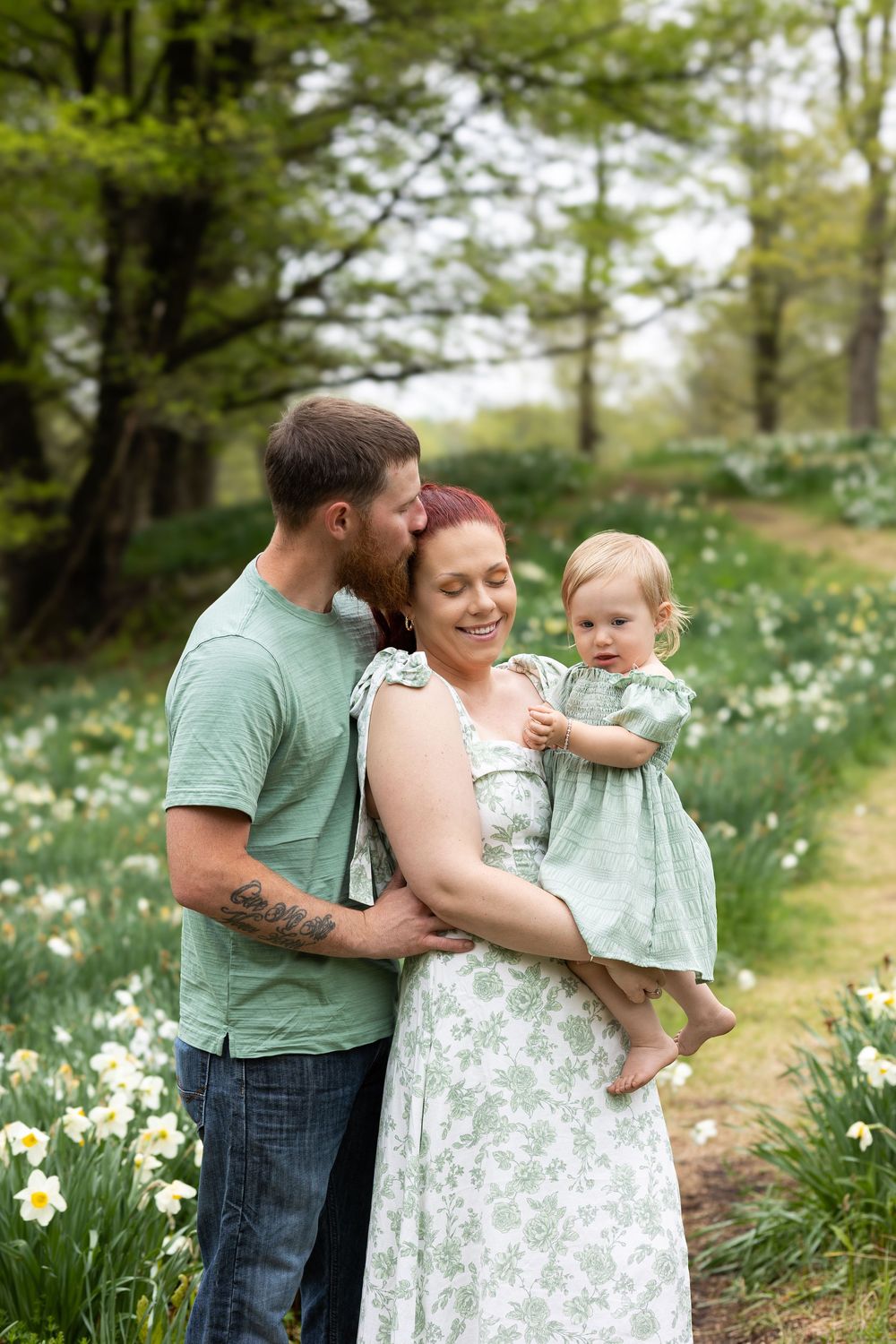 Family embraces in a tender moment among spring daffodils wearing coordinating mint green and white outfits.